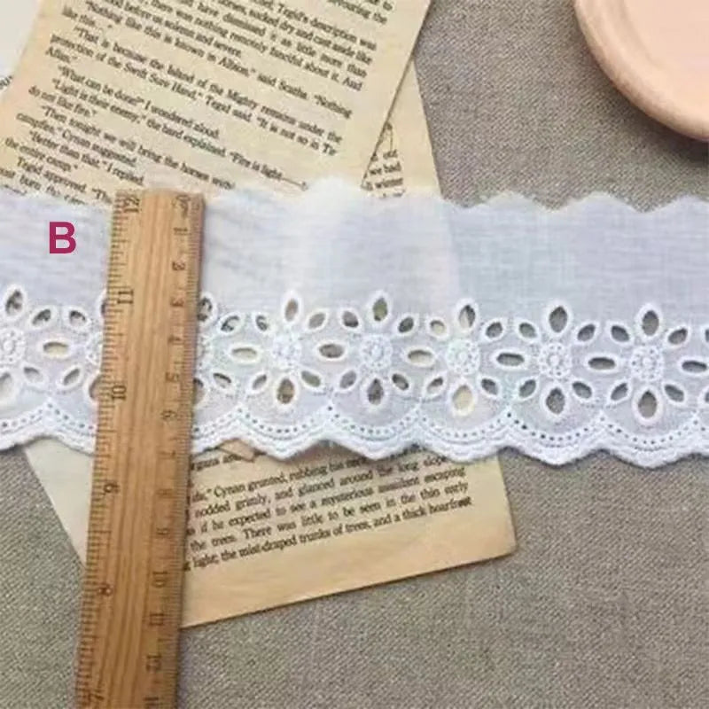 Roll of white cotton embroidery lace trim with cutout pattern, showing width variations.
