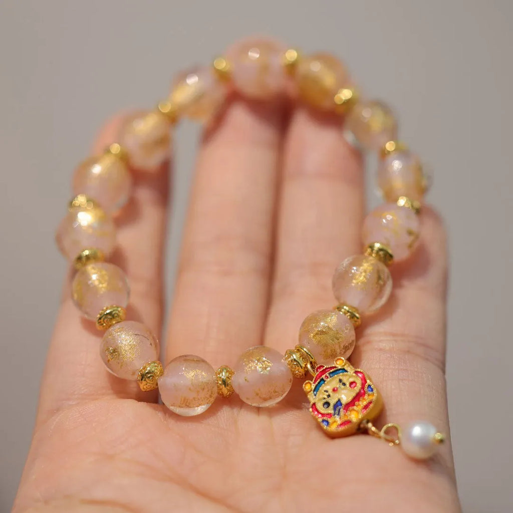 Women's ethnic style bracelet with gold foil designs on red and pink coloured glass glaze, featuring geometric shapes and charms.