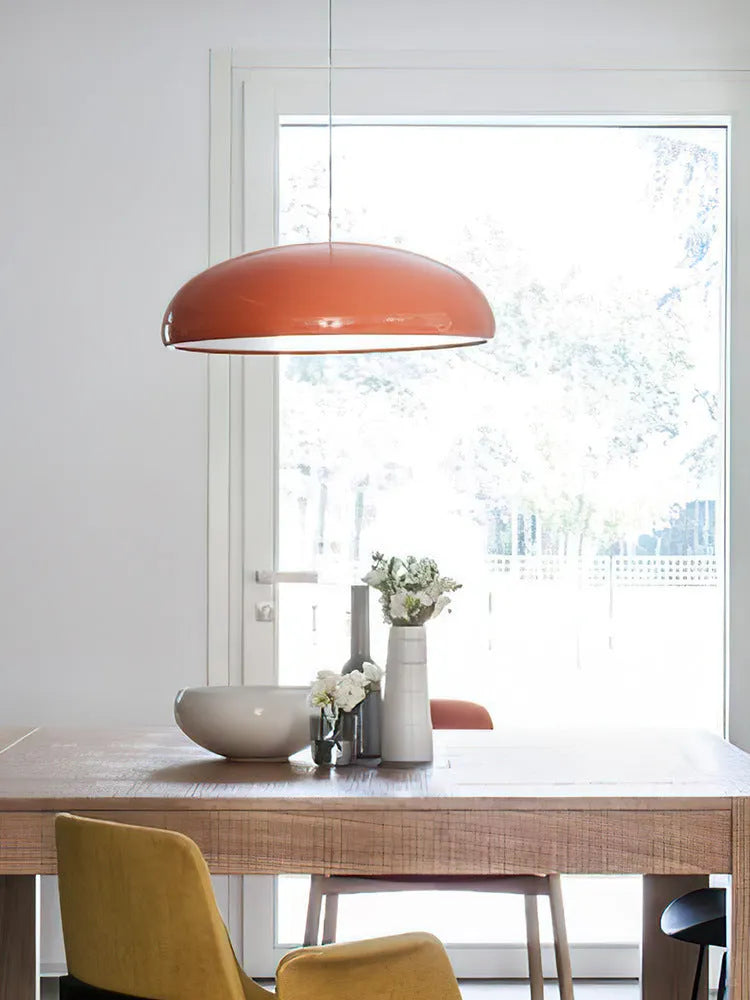Modern Danish orange iron pendant lamp with adjustable cable over a restaurant dining table.