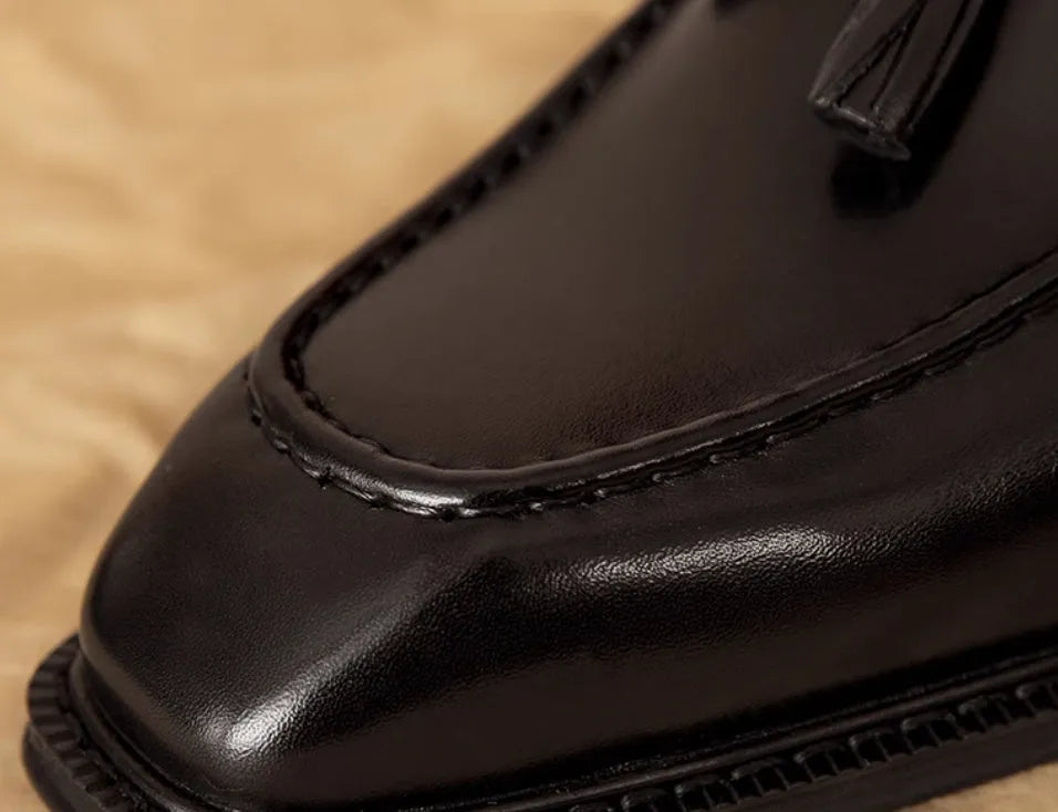 Men's black genuine leather loafers with fringe detail and a rubber sole, shown from a side angle.