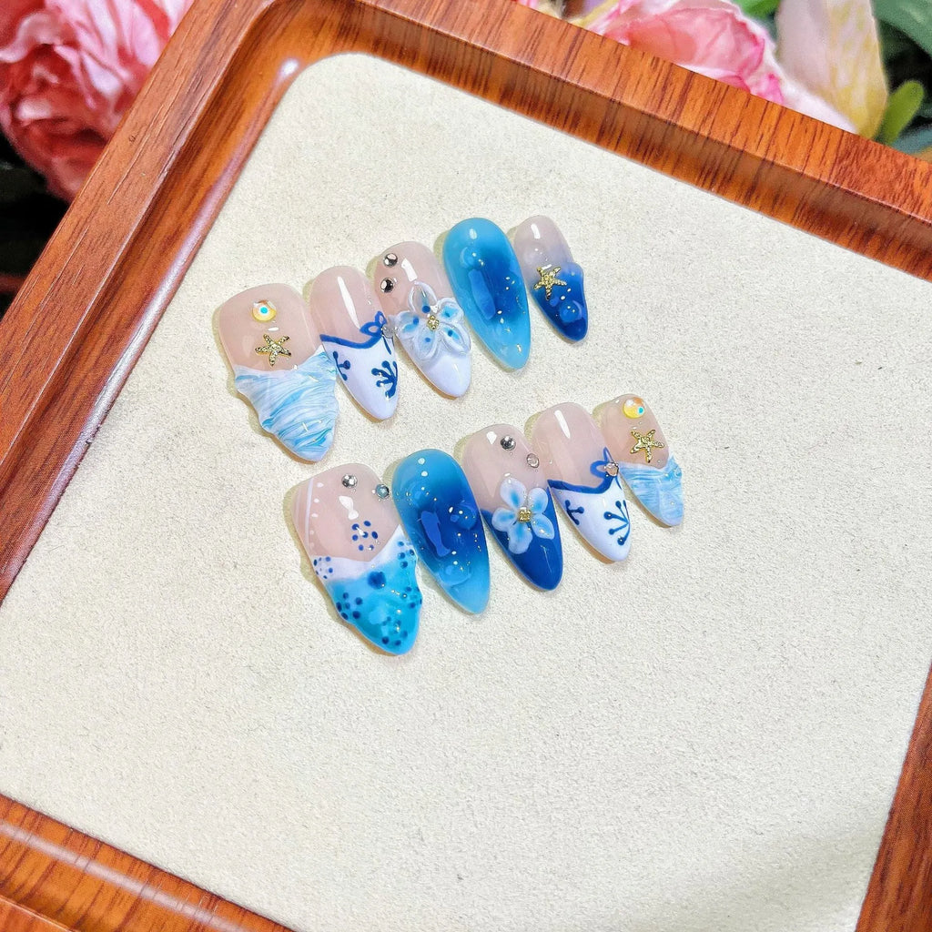 Set of blue false nails with hand-painted colour and carved summer ice design, laid out on a surface.
