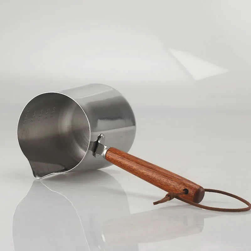 Stainless steel coffee milk jug with wooden handle and measuring scale for latte art.