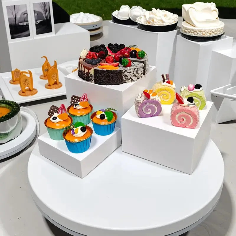 Set of six white plastic cube dessert display stands arranged on a tabletop.