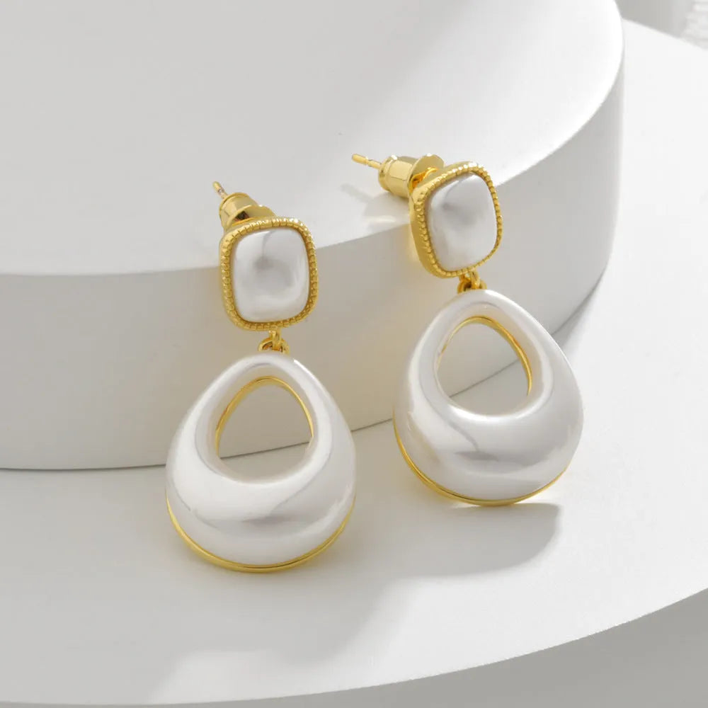 Gold coloured drop shaped earrings with a central imitation pearl, shown on a white background.