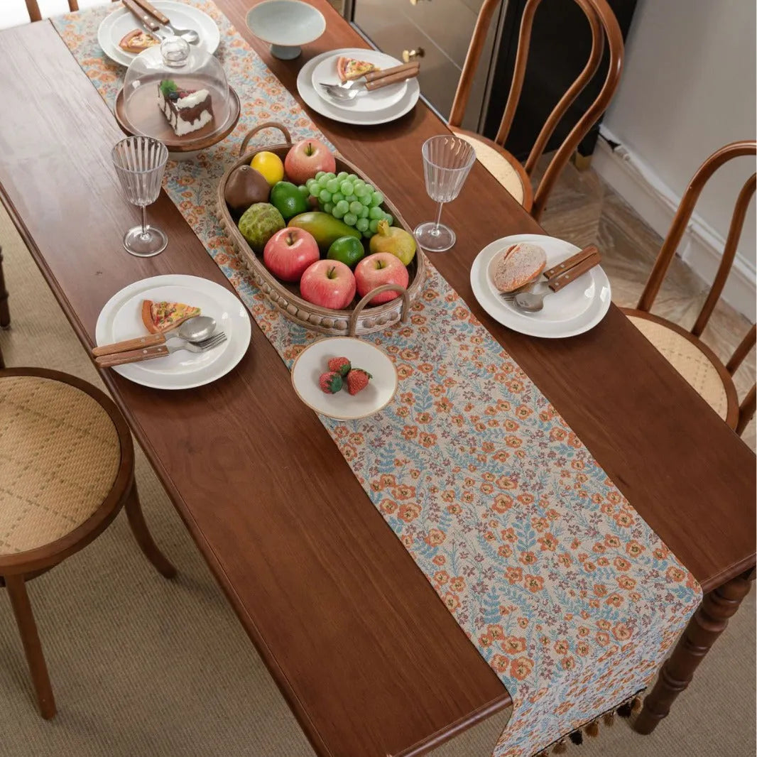 Beige jacquard table runner with long tassels and a woven flowers and leaves pattern draped over a table.