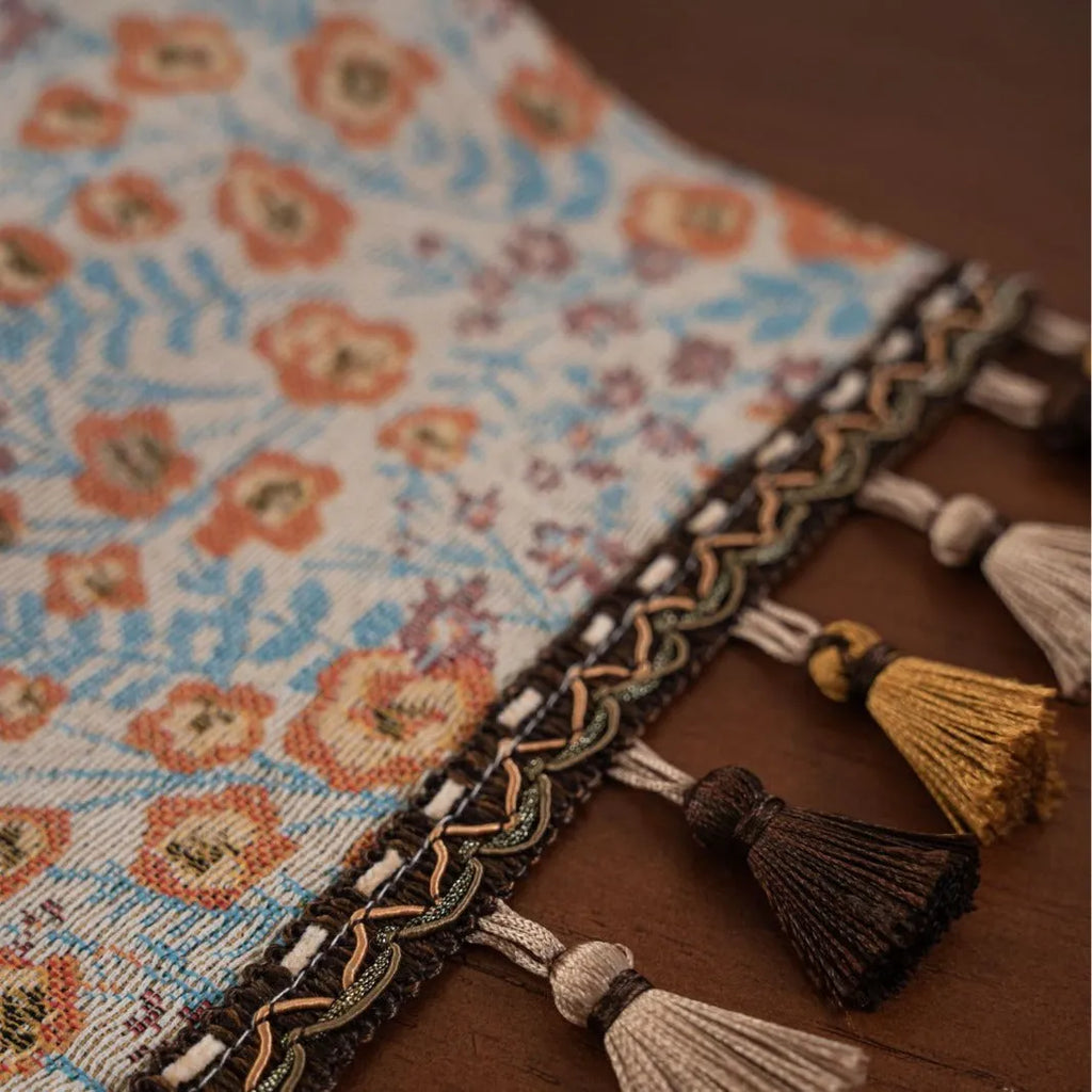 Beige jacquard table runner with long tassels and a woven flowers and leaves pattern draped over a table.