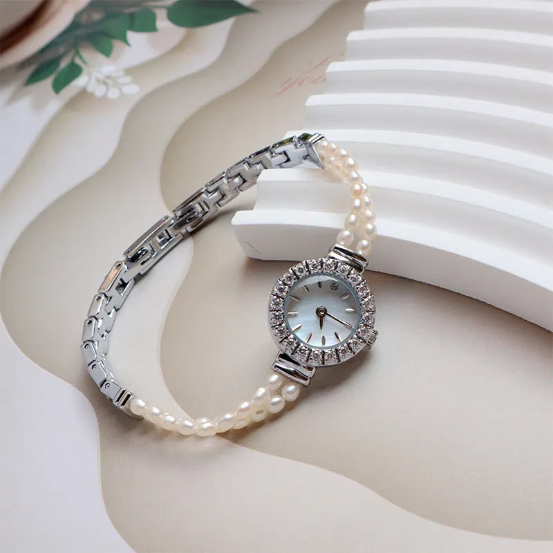 Light gold women's bracelet watch with freshwater pearls, round 18mm dial, and stainless steel strap.