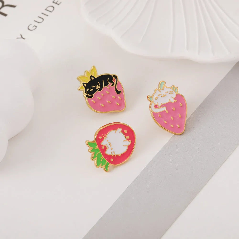 Close-up of a cute cat strawberry dripping oil cake design alloy metal brooch on a fabric background.