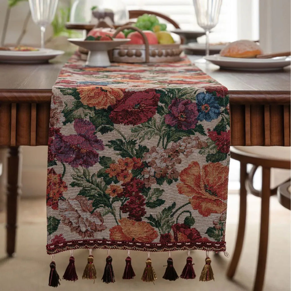 Beige jacquard table runner with long tassels and a woven flowers and leaves pattern draped over a table.