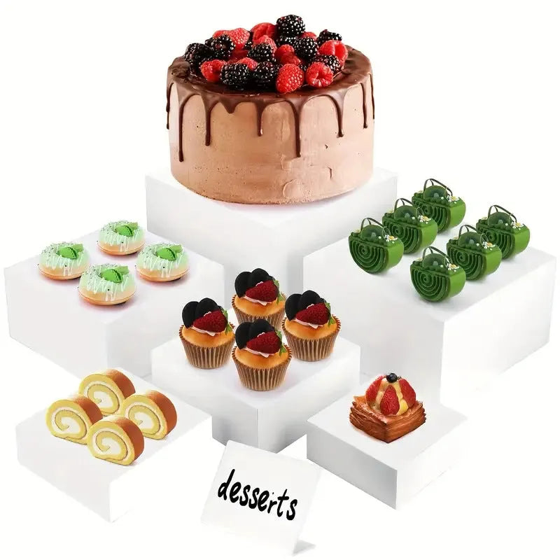 Set of six white plastic cube dessert display stands arranged on a tabletop.