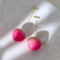 A pair of peach-shaped acrylic earrings on copper posts, shown in small and large size options.