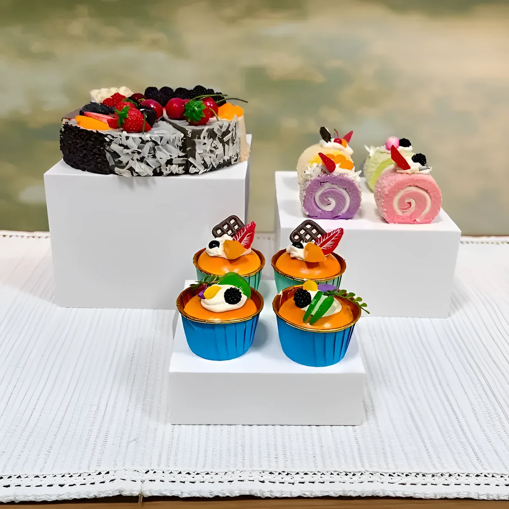 Set of six white plastic cube dessert display stands arranged on a tabletop.