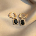 Close-up of black geometric quadrilateral stud earrings with zircon stones on a French court wire.
