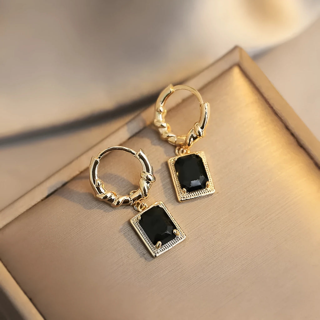 Close-up of black geometric quadrilateral stud earrings with zircon stones on a French court wire.