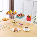 Set of six white plastic cube dessert display stands arranged on a tabletop.