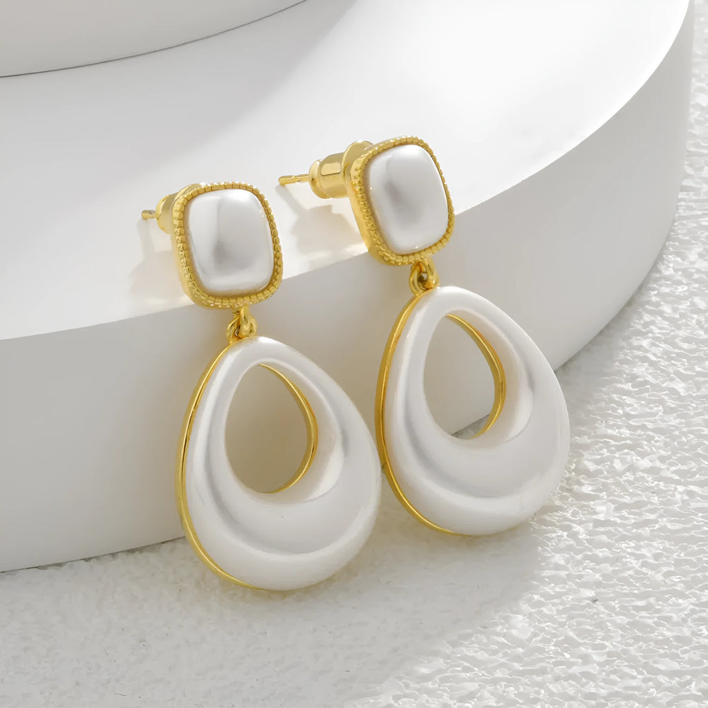 Gold coloured drop shaped earrings with a central imitation pearl, shown on a white background.