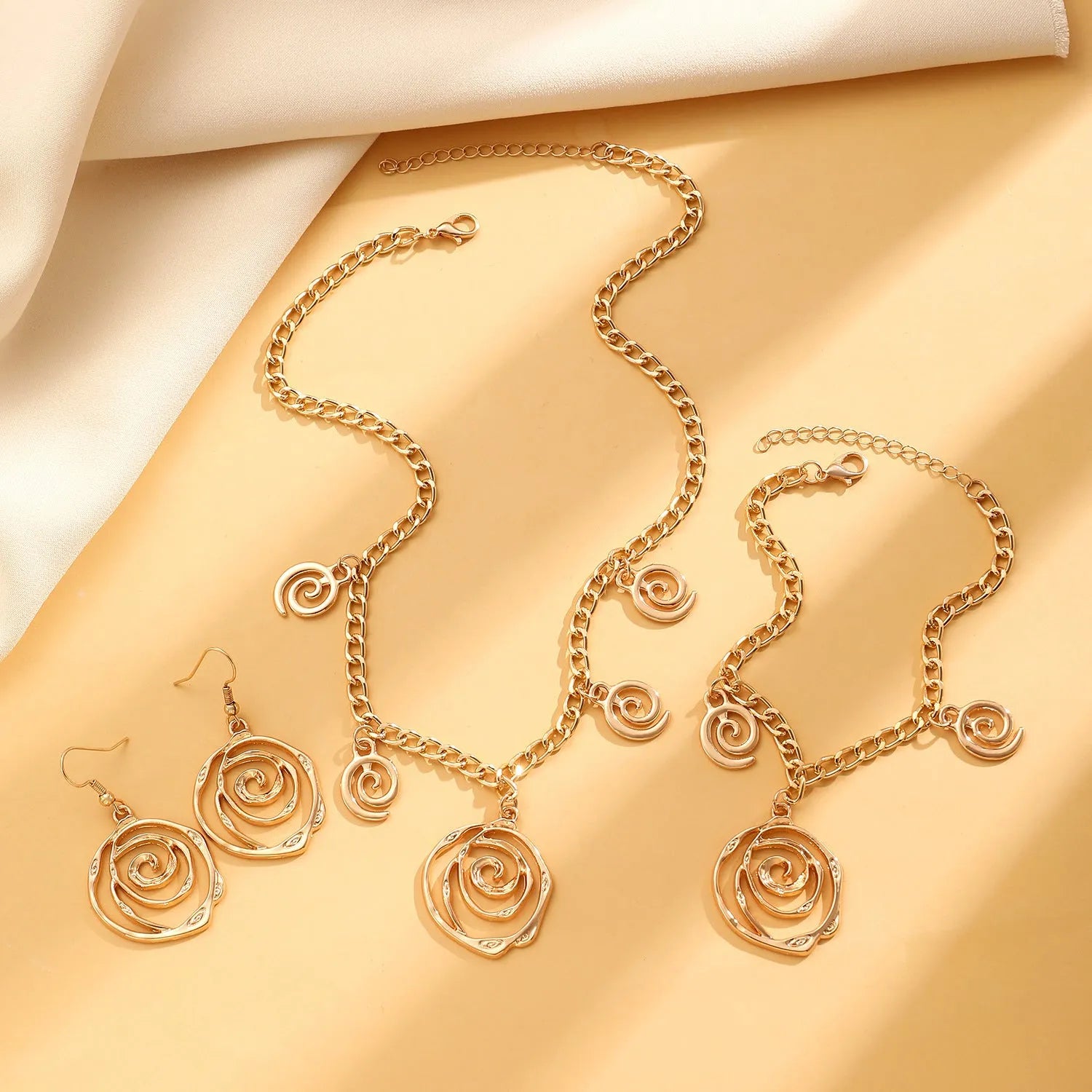 Geometric spiral donut jewellery set showing necklace, bracelet, and earrings in gold electroplated finish
