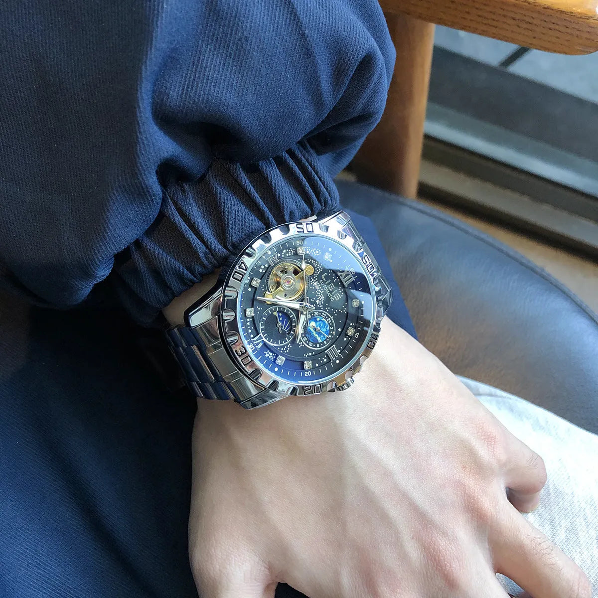 Men's silver automatic watch with black leather strap and transparent case back.