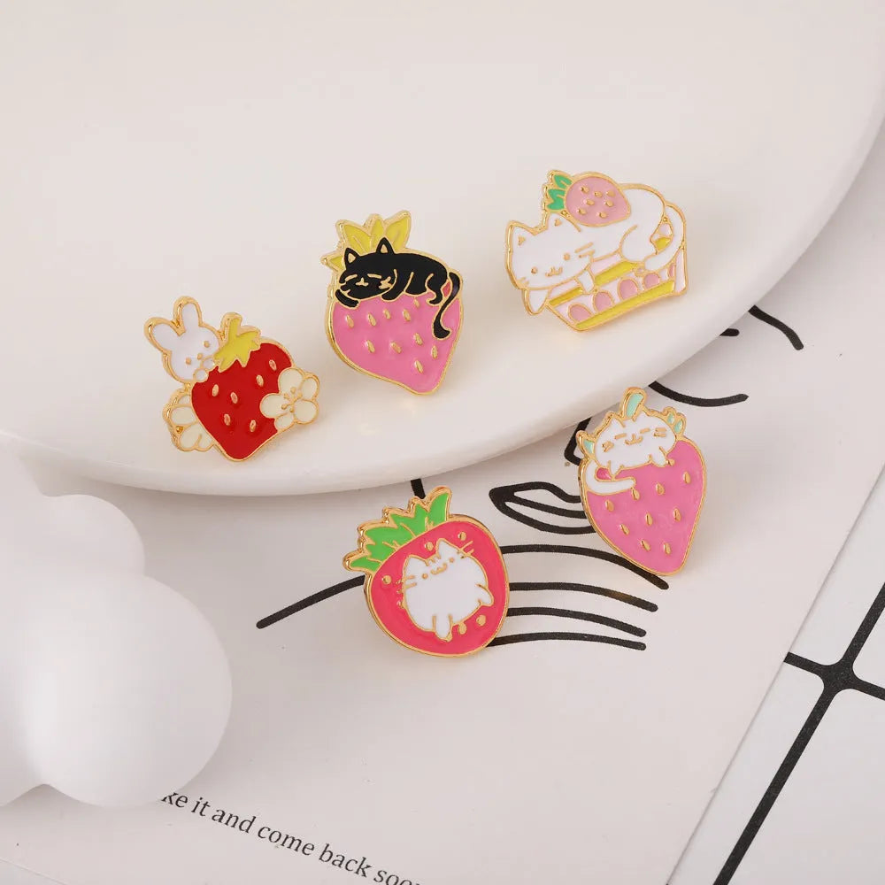 Close-up of a cute cat strawberry dripping oil cake design alloy metal brooch on a fabric background.