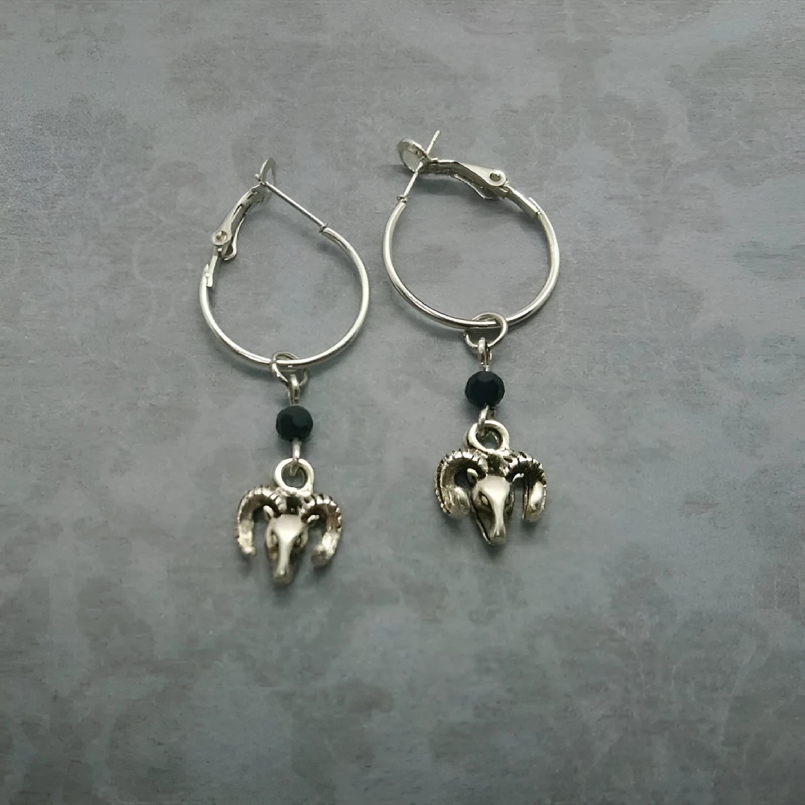 A pair of silver-coloured alloy round ring hoop earrings on a plain background.