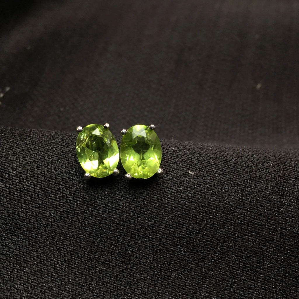 Close-up of grass green natural olivine faceted stud earrings in S925 silver geometric setting.