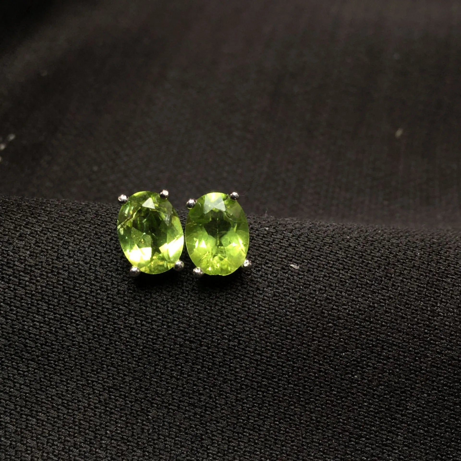 Close-up of grass green natural olivine faceted stud earrings in S925 silver geometric setting.