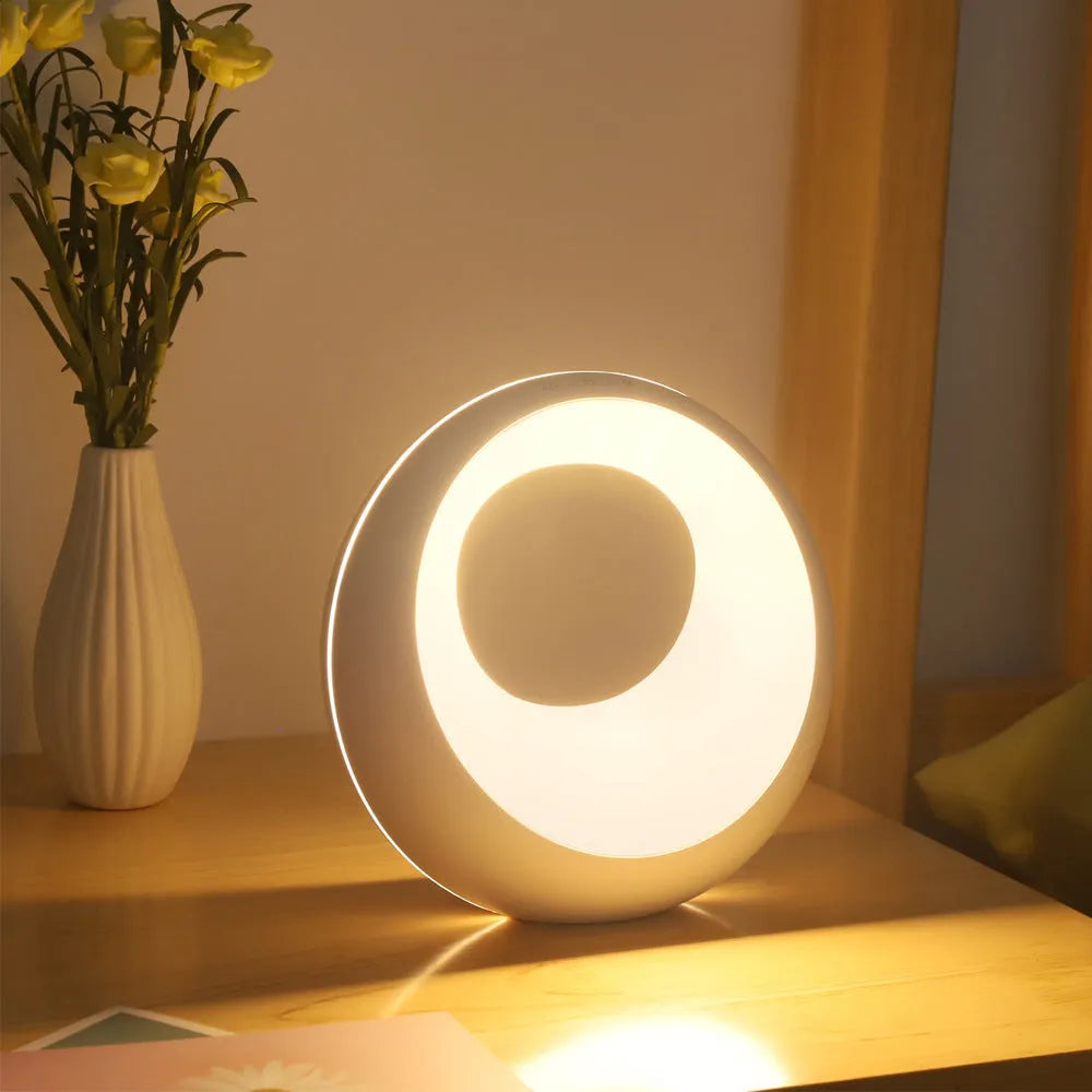 Small white RGB colour changing night lamp with remote control on a wooden desk.