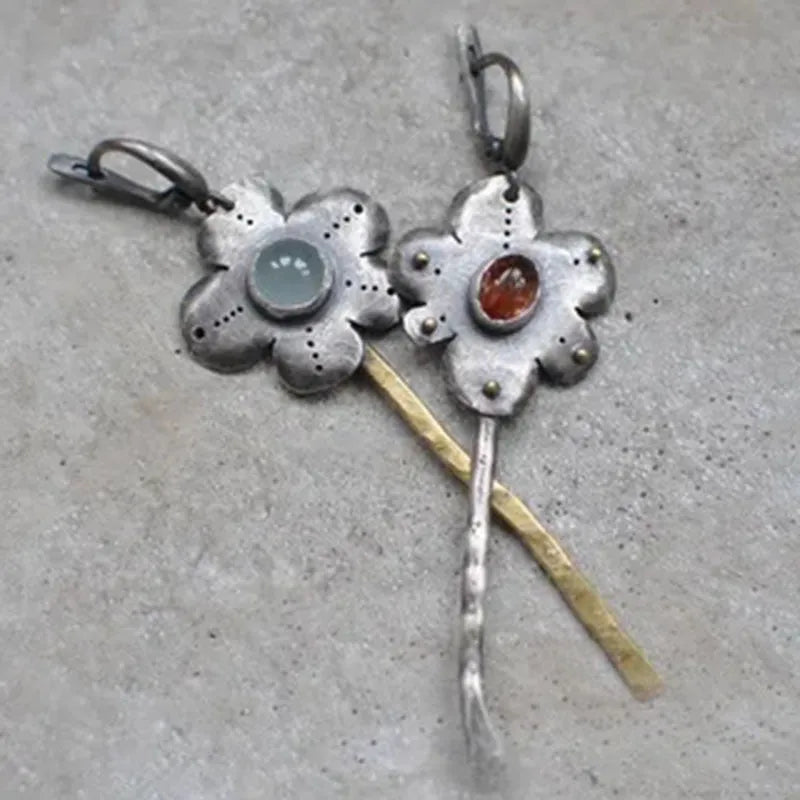 A pair of long, geometric flower-shaped retro earrings in two contrasting metallic colours with an asymmetrical design.