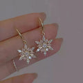 Gold alloy snowflake drop earrings with clear zircon centre on a white background