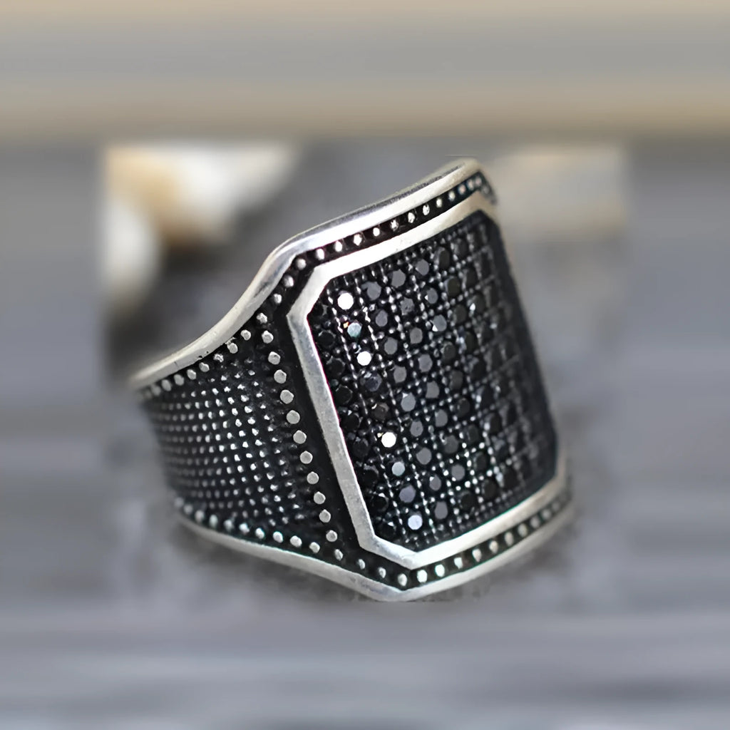 Black alloy ring with copper inlay and a central zircon stone, shown on a finger.