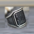 Black alloy ring with copper inlay and a central zircon stone, shown on a finger.
