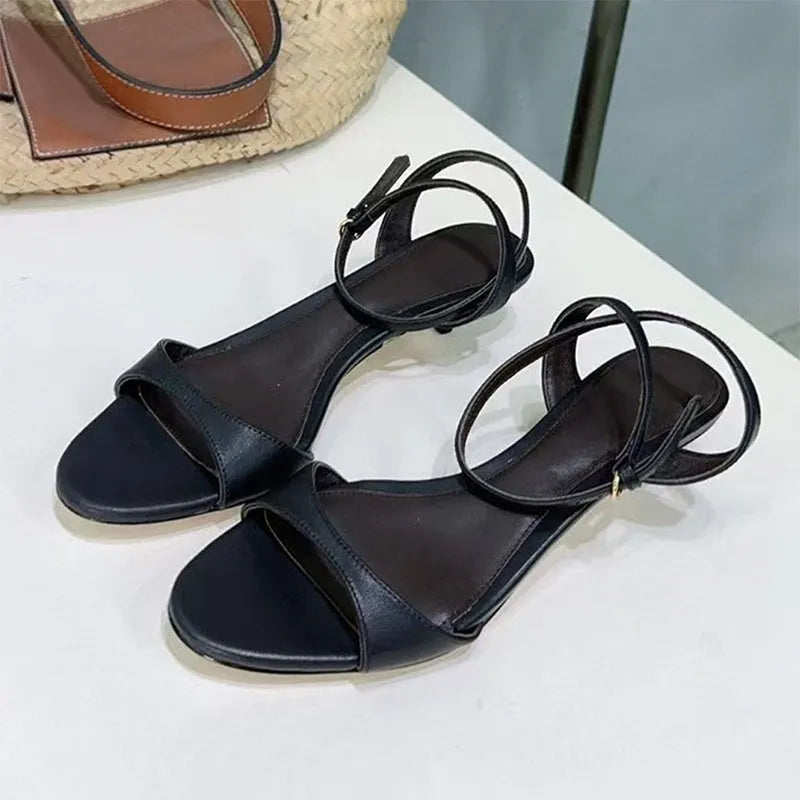 Women's black leather open-toe sandals with a low kitten heel and buckle strap, shown from the side.