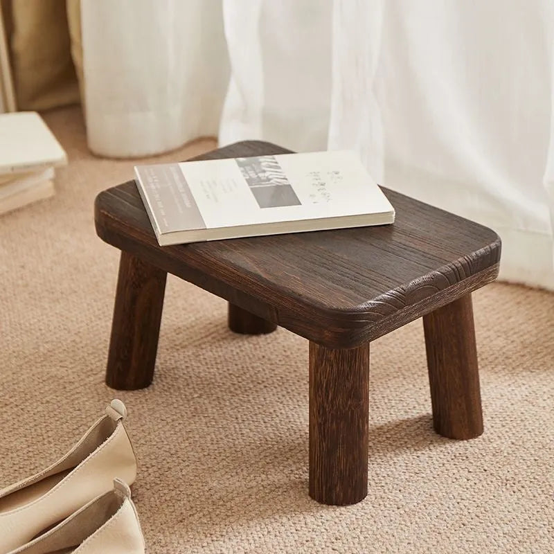 A rustic distressed wooden stool with bracket legs, used as a shoe changing bench in a hallway.