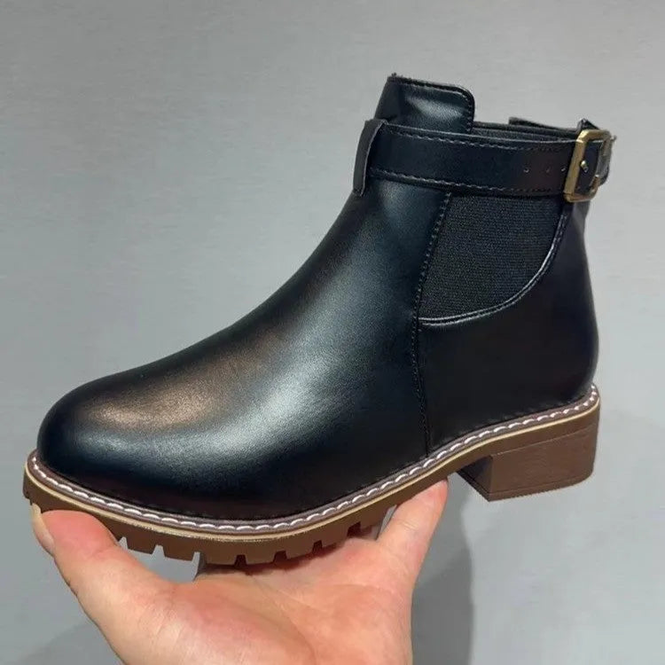 Black round toe ankle boot with a silver belt buckle decoration on the side.
