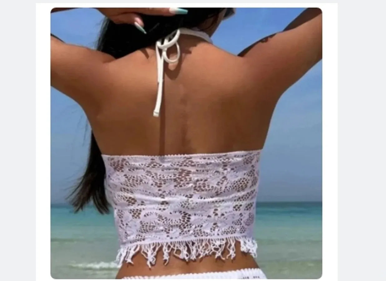 Women's white two-piece bikini with lace cover-up skirt and tassel trim on a beach.