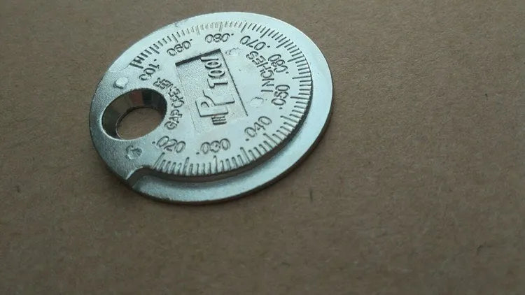 Round zinc alloy spark plug gauge with dual scales on a white background