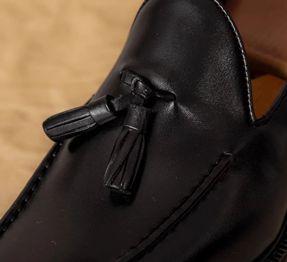 Men's black genuine leather loafers with fringe detail and a rubber sole, shown from a side angle.
