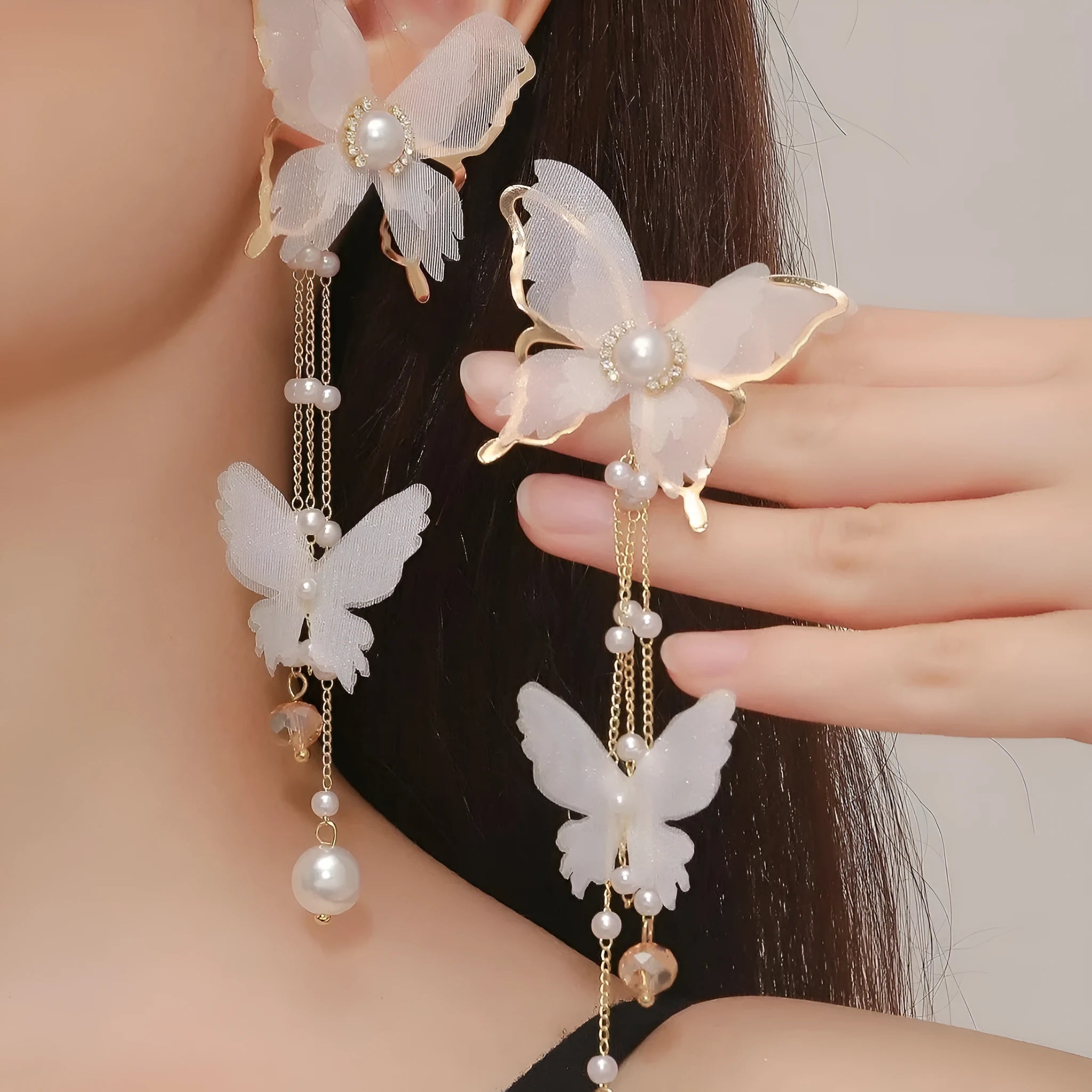Close-up of white butterfly-shaped earrings with dangling lace tassels and sparkling pearl rhinestone details.
