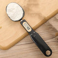 White electronic digital spoon scale with LCD display on a kitchen counter.