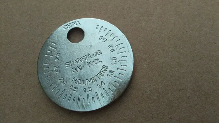 Round zinc alloy spark plug gauge with dual scales on a white background