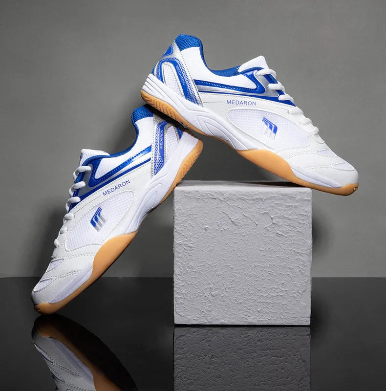 White and blue table tennis sneakers with synthetic leather upper and rubber sole on a court surface.