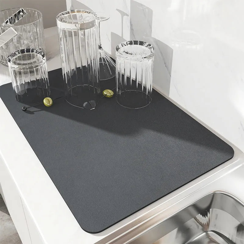 Square black kitchen drain mat with rubber backing placed under coffee machine on countertop