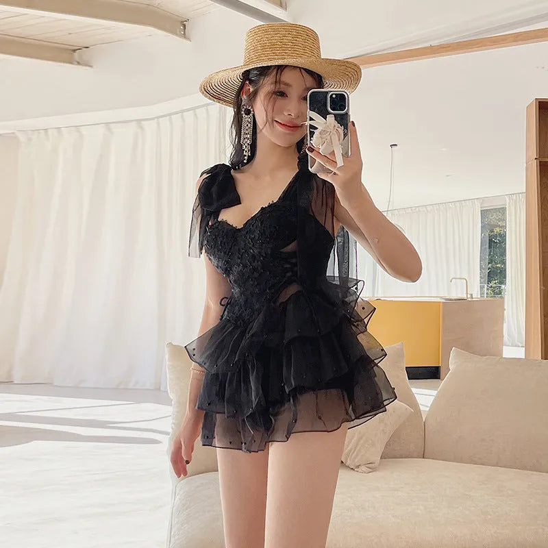 Black one-piece swimsuit with gathered chest detail on a mannequin, showing sleeveless design.