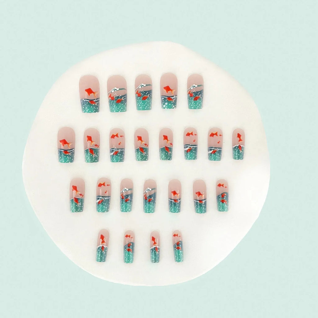 Mid-square blue glaze goldfish nail art pieces with armour design and jelly glue finish on a table