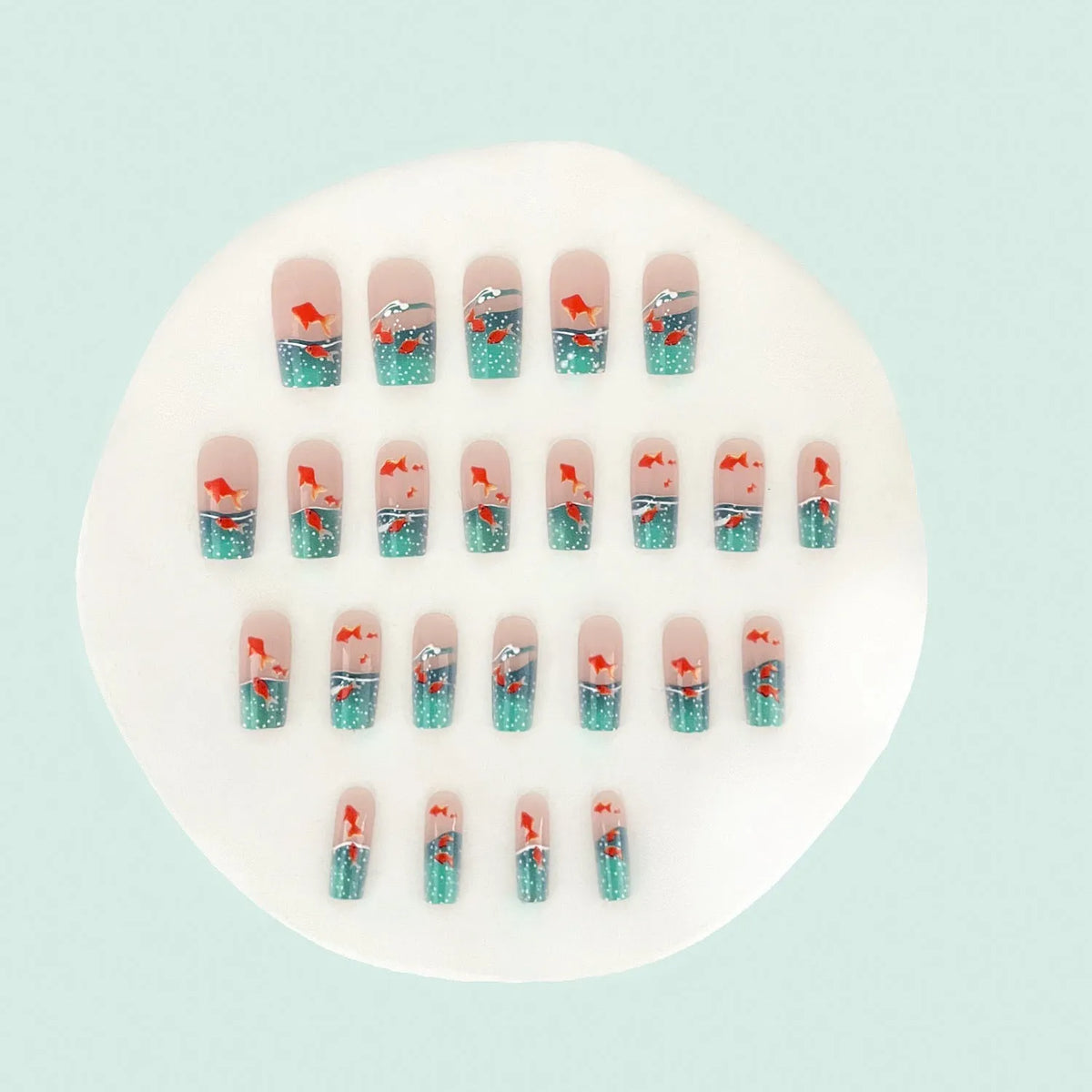 Mid-square blue glaze goldfish nail art pieces with armour design and jelly glue finish on a table