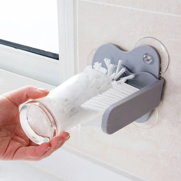 Grey 2-in-1 cup scrubber with double-sided bristles and three suction cups on a white surface