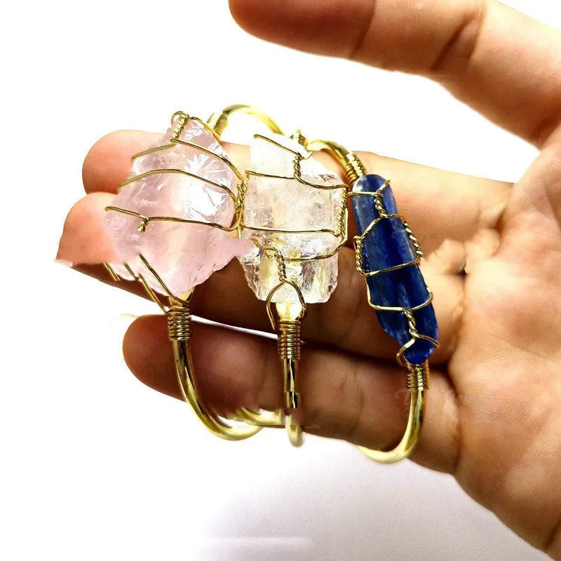 Natural rough stone crystal bracelet with gold geometric winding on a wrist.