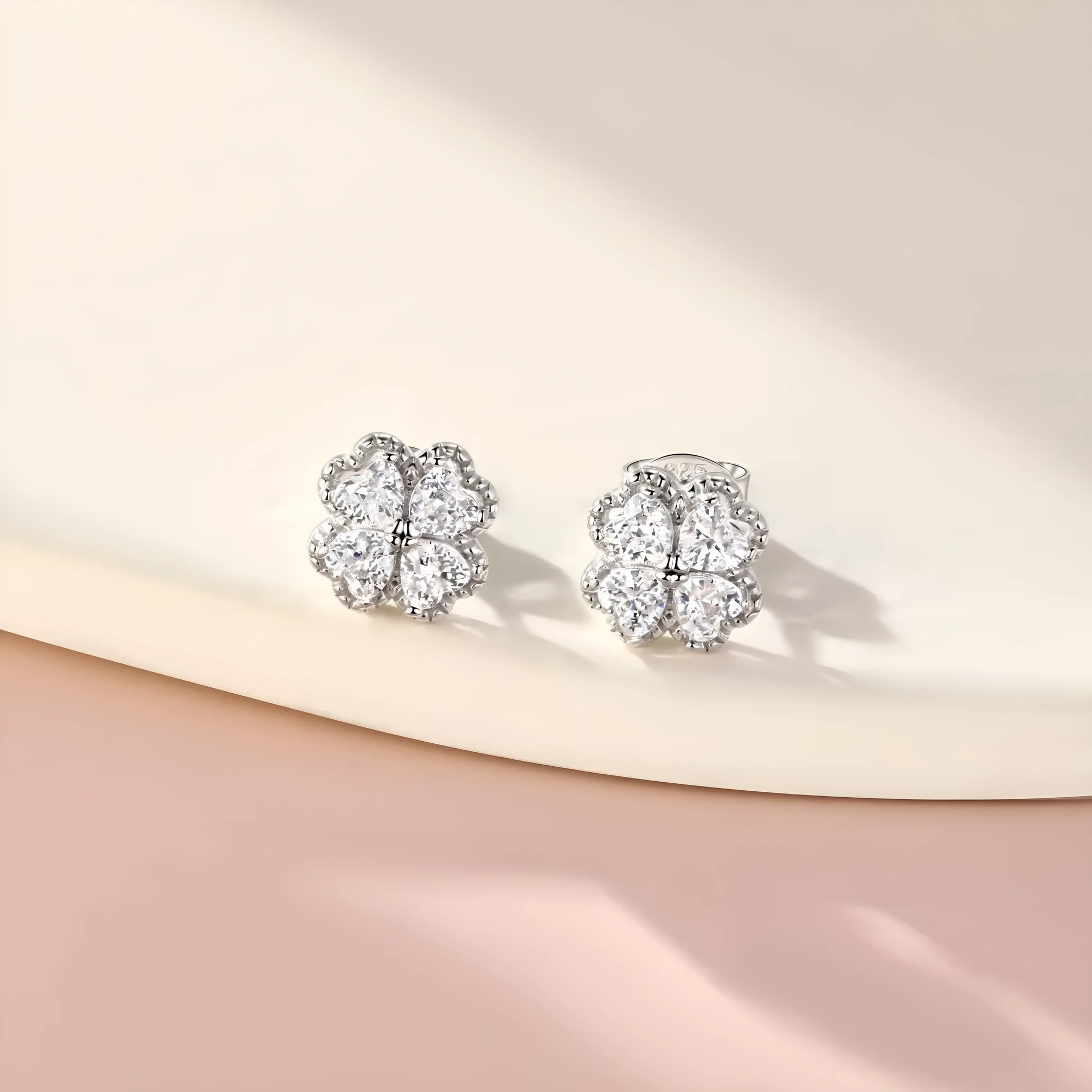 A pair of 925 silver earrings with a four-leaf clover charm and heart-shaped zircon stones in white gold colour.