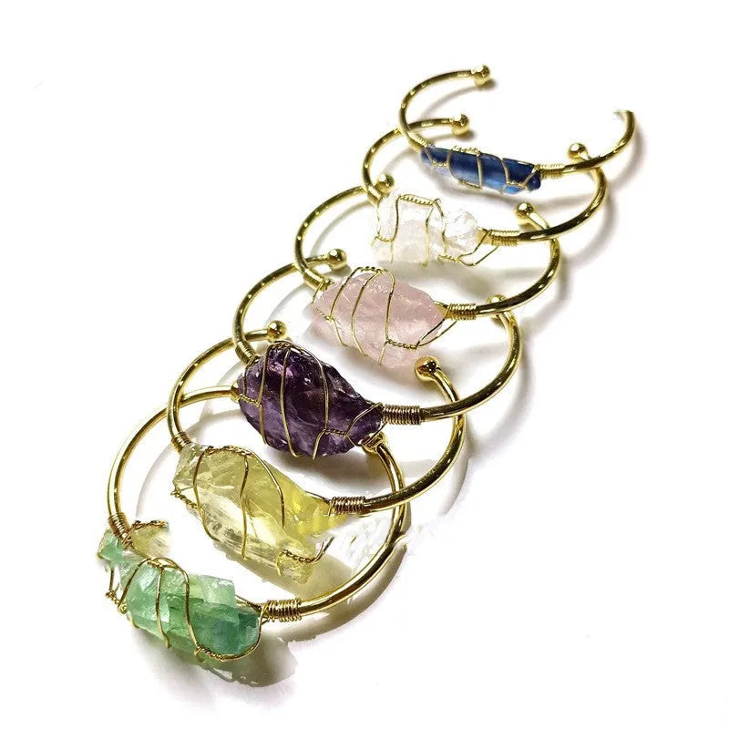 Natural rough stone crystal bracelet with gold geometric winding on a wrist.