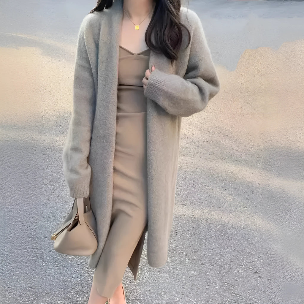 A woman wearing a khaki coloured, mid-length V-neck knitted cardigan with long sleeves.